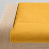 Primer pla d'un coixí groc modern sobre mobles de fusta elegants, que mostren materials i artesania d'alta qualitat.