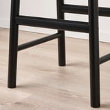 Tamboret de bar de metall negre amb seient de bedoll resistent i barana transversal, que mostra una artesania robusta.