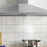 Campana d'acer inoxidable amb llum led sobre paret de rajoles, extractor a la vista.