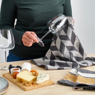 Dues tovalloles de cuina penjants; un ratllat gris i daurat, l'altre geomètric gris i blanc. Fabricat en cotó absorbent i jute.