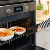 Persona que utilitza guant de forn de silicona per treure els plats del forn. El guant protegeix les mans i proporciona adherència.