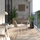 Balcó modern amb cadira SEGERÖN de vímet, color natural, estructura d'acer, seient encoixinat. Teló de fons de paret de formigó, vegetació i decoració minimalista.