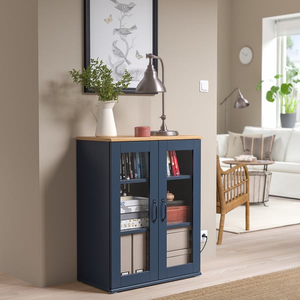 Armari SKRUVBY blau amb portes de vidre, tiradors rústics i planta a prop.