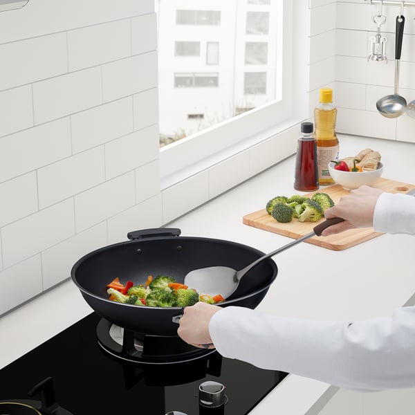 Persona cuinant verdures al wok a la cuina moderna amb espàtula SLITSTARK, a prop de la finestra.