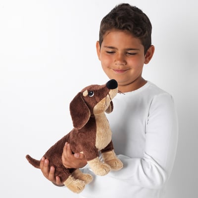 Un nen somriu mentre sosté una joguina de teckel suau, marró i de peluix; Perfecte per abraçar-se i jugar.