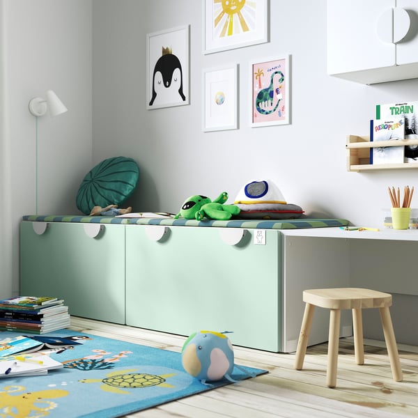 Habitació infantil amb banc verd SMÅSTAD que emmagatzema joguines, catifa de colors, tamboret de fusta i art mural. Disseny brillant i lúdic, perfecte per jugar.