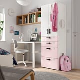 Una habitació infantil, un armari SMÅSTAD blanc amb calaixos rosa, un escriptori amb un ordinador portàtil i una motxilla. L'armari té ganxos i calaixos.