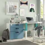 Configuració moderna d'oficina a casa amb un escriptori blanc i blau amb calaixos, una cadira grisa, una motxilla, un ordinador portàtil, auriculars i art mural de colors.