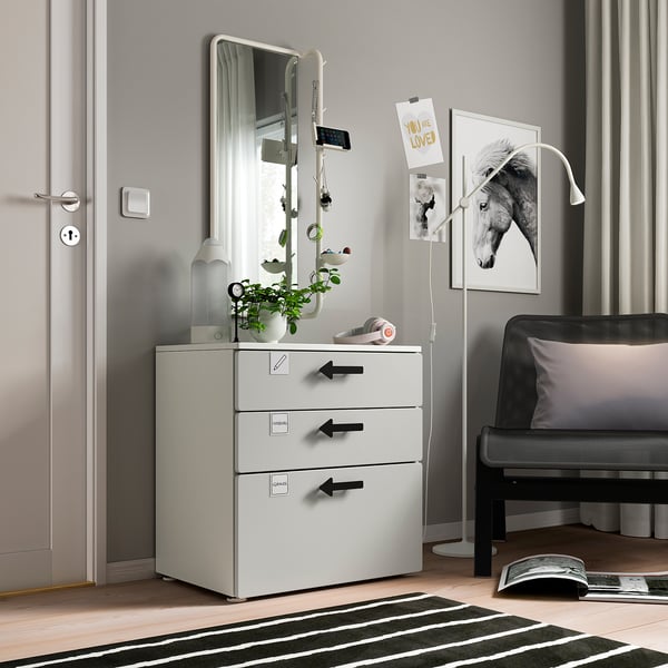 Moble d'emmagatzematge infantil blanc modern amb tres calaixos, un mirall i objectes decoratius.