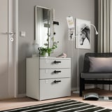 Moble d'emmagatzematge infantil blanc modern amb tres calaixos, un mirall i objectes decoratius.