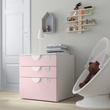Habitació petita amb calaixos d'emmagatzematge de color rosa clar, llum blanca i prestatges penjants que mostren joguines.