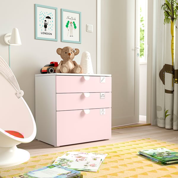 Habitació infantil amb cofre SMÅSTAD de color rosa clar. Un ós de peluix i blocs a la part superior, catifa de colors amb llibres. Cadira blanca, estampats a la paret.