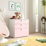 Habitació infantil amb cofre SMÅSTAD de color rosa clar. Un ós de peluix i blocs a la part superior, catifa de colors amb llibres. Cadira blanca, estampats a la paret.