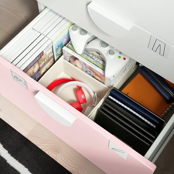Tres calaixos oberts d'un cofre SMÅSTAD rosa, amb accessoris de videojocs, llibres i una llibreta.