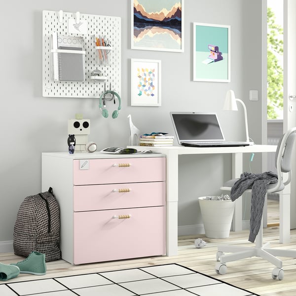 Espai de treball domèstic amb calaixos SMÅSTAD rosa, tauler perforat, escriptori, ordinador portàtil, llibres i decoració personal.
