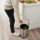 Persona que llença enciams en una paperera d'acer inoxidable amb un mànec a la part posterior, col·locada sota un taulell.