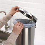 Persona que col·loca una bossa de plàstic dins d'una paperera de pedal d'acer inoxidable amb nansa, apta per a residus o reciclatge a la cuina o al bany.
