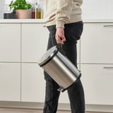 Persona que sosté una paperera de pedal d'acer inoxidable amb mànec a la cuina.