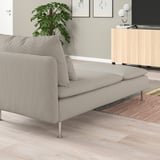 Una elegant chaise SÖDERHAMN de color gris clar amb seient i respatller encoixinats, col·locada contra una paret amb una catifa vegetal i de colors a prop.