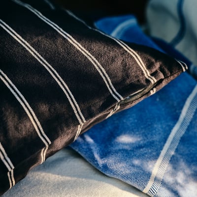 Veig un coixí de ratlles blanques i negres, de forma rectangular. Té un aspecte acollidor i elegant amb el seu disseny lineal.