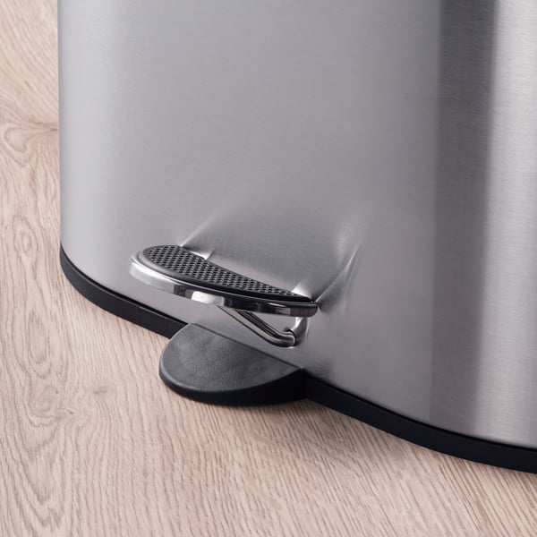 Contenidor de pedal d'acer inoxidable amb mecanisme de tancament suau sobre terra de fusta.