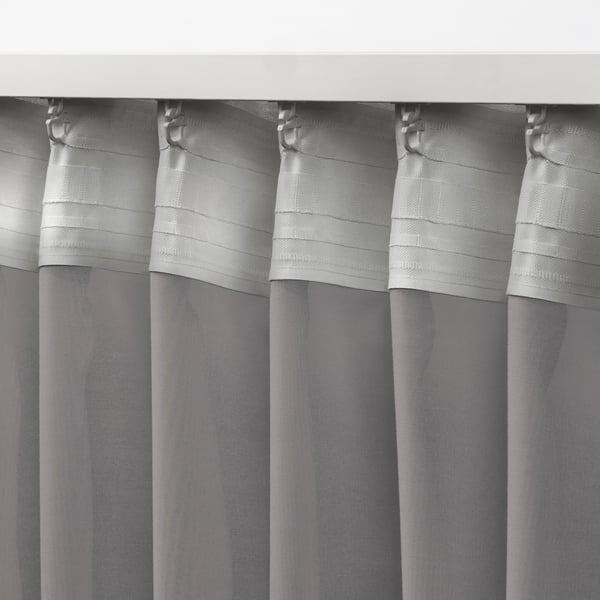 Cortines grises transparents amb ganxos metàl·lics penjants, difonent la llum del dia, ideals per a tractaments de finestres en capes.
