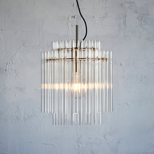 Un candelabre modern amb cilindres de vidre transparent penja d'un ganxo metàl·lic, emetent llum càlida.