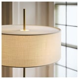 Primer pla d'un elegant llum de peu amb una pantalla beix i textura i un suport de llautó, que reflecteix materials d'alta qualitat i un disseny elegant.