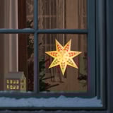 Llum estrella escandinava a la finestra amb flors vermelles, que brilla càlidament, creant un ambient interior acollidor amb vistes a la neu.