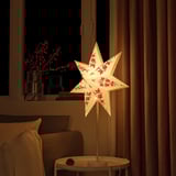 Acollidor racó de la sala d'estar amb una pantalla d'estrella amb estampat de flors vermelles d'IKEA, que il·lumina el sofà marró i la manta de punt.
