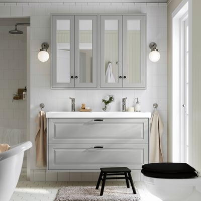 Bany gris modern amb doble lavabo, accessoris cromats i flors.