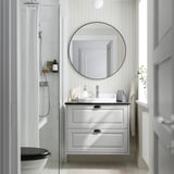 Tocador de bany gris modern, mirall rodó, lavabo i vàter blancs. Rajoles i dutxa.