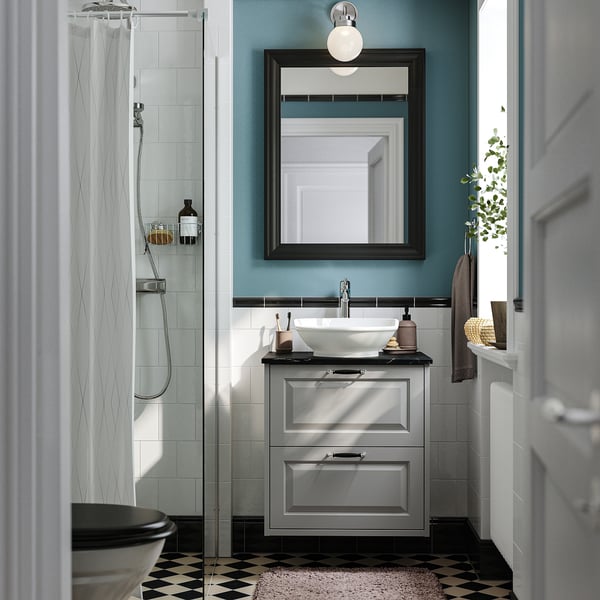 Bany modern: tocador TÄNNFORSEN gris, lavabo rodó, mirall negre, dutxa arran de terra, paret turquesa, rajoles blanques.