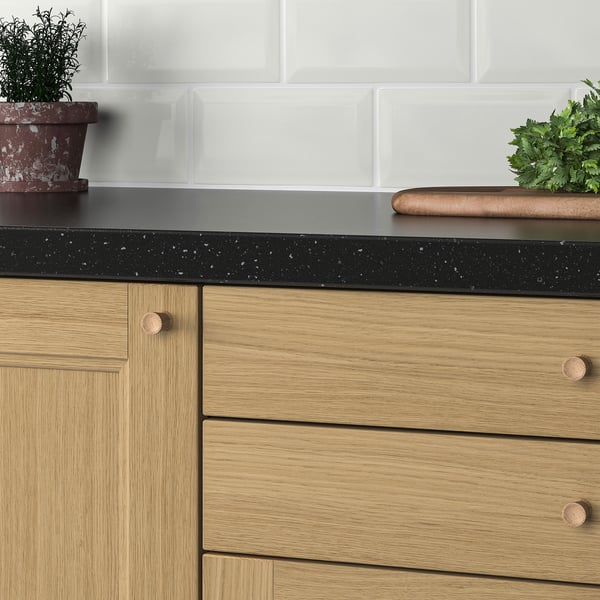 Calaixos d'armaris de fusta amb taulell tacat negre, backsplash de rajoles blanques i herbes en test.