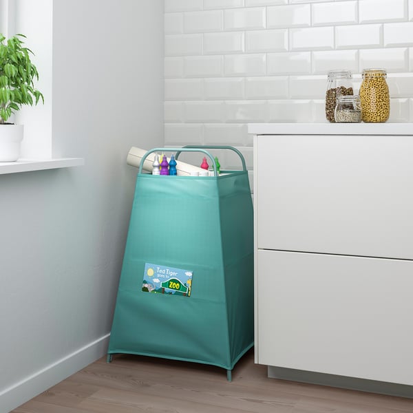 Bossa d'emmagatzematge de joguines verdes TIGERFINK a l'habitació amb armari blanc, pots d'estampat de lleopard i planta. Conté diverses joguines infantils.