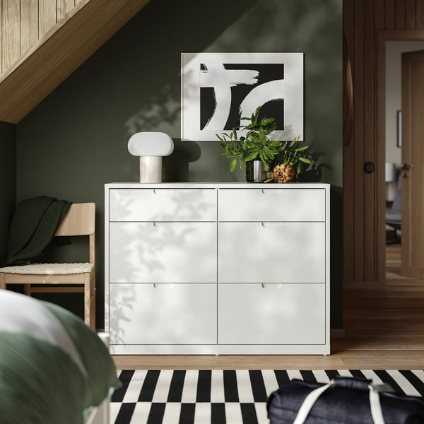 Elegant cofre blanc TONSTAD, habitació moderna. Sis calaixos, art botànic, llum, banc, paret verda.