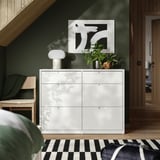Elegant cofre blanc TONSTAD, habitació moderna. Sis calaixos, art botànic, llum, banc, paret verda.