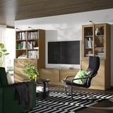 Sala d'estar moderna: TV negra, prestatges de fusta, balancí negre, planta, catifa blanca i negra, il·luminació suau.