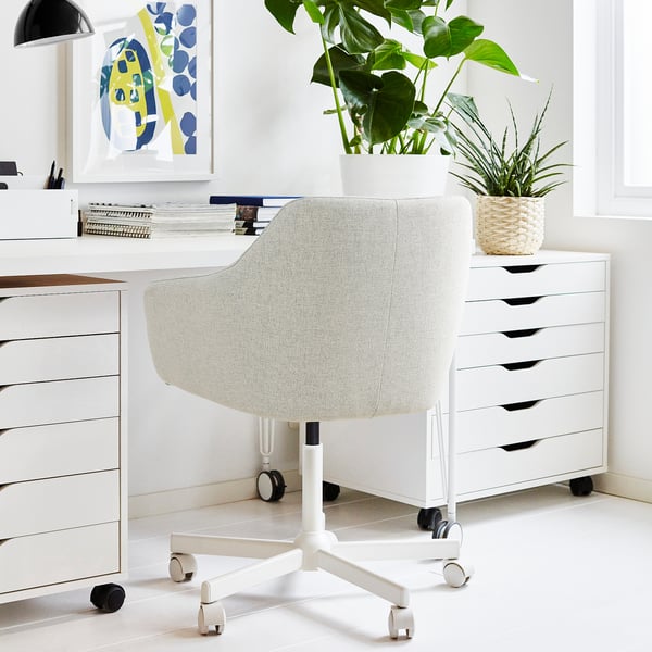 Configuració moderna d'oficina a casa amb cadira TOSSBERG, blanca. La cadira és ergonòmica amb rodes, col·locada entre calaixos blancs i escriptori. Les plantes afegeixen vegetació.