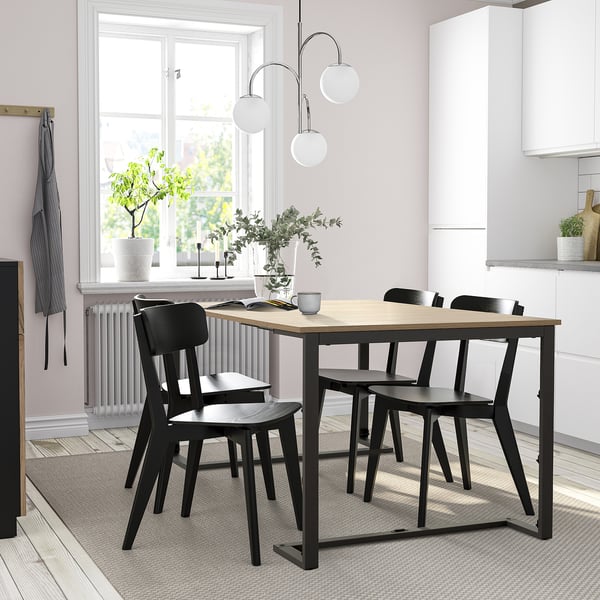 Configuració moderna de menjador amb taula i cadires negres TRÄKUMLA, disseny elegant, capacitat per a quatre, situat a prop d'una finestra lluminosa.