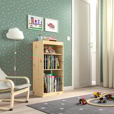 Habitació infantil amb prestatgeria de fusta clara TROFAST amb llibres i joguines. Paper pintat brillant, catifa i llum de peu. Cotxes de joguina i cadira visibles.