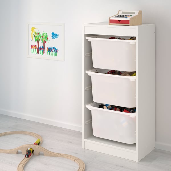 Traster TROFAST blanc amb tres calaixos plens de joguines, al costat de vies de tren de fusta.