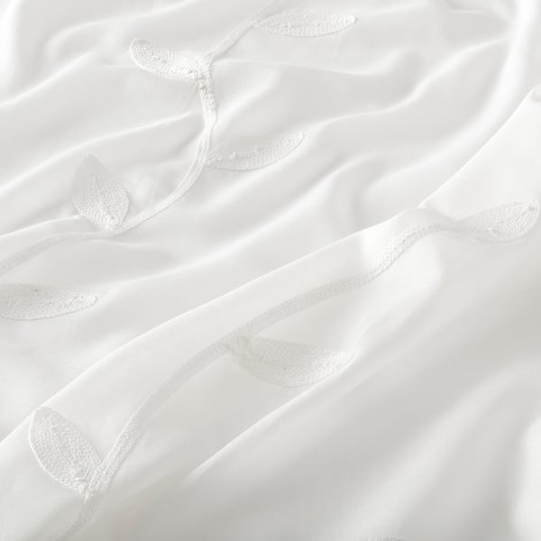 Les cortines blanques transparents amb estampats de fulles complexos, finament detallades, pengen amb elegància, oferint una visió de llum natural i una subtil privacitat.