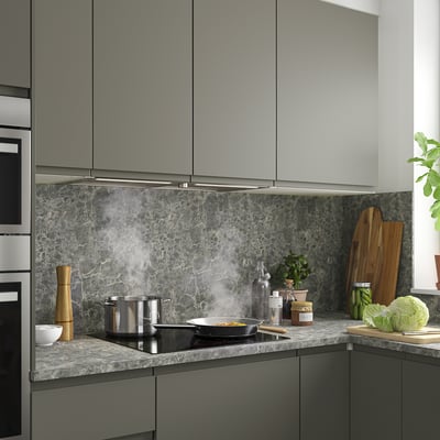 Cuina moderna amb armaris grisos, placa negra, campana inoxidable, backsplash de marbre i estris de taulell i vegetació.