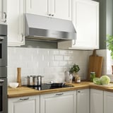 Cuina amb campana d'acer inoxidable, placa de cuina negra, backsplash de metro blanc i taulells de fusta.