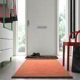 Catifa taronja i marró VÄGOMRÅDE al passadís, prop de la porta blanca i la cadira vermella.