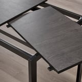 Taula de menjador extensible amb una fulla emmagatzemada a sota. Les potes de metall negre suporten la part superior de fusta grisa.