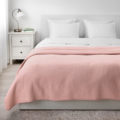 Acollidor dormitori amb cobrellit de cotó VÅRELD rosa clar sobre llit de matrimoni. Tauleta de nit blanca, terra de fusta, catifa.