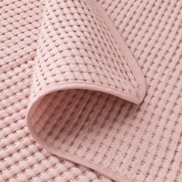 Un primer pla d'un cobrellit de cotó teixit suau de color rosa clar que mostra el seu patró texturitzat i les costures fines.