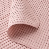 Un primer pla d'un cobrellit de cotó teixit suau de color rosa clar que mostra el seu patró texturitzat i les costures fines.